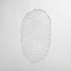 Minimalistic artwork featuring the delicate outline of a fingerprint subtly cut out from a smooth white surface. The cut creates a faint, intricate pattern that contrasts gently with the surrounding negative space, inviting close inspection of the fine lines and curves that form the fingerprint's unique texture.
