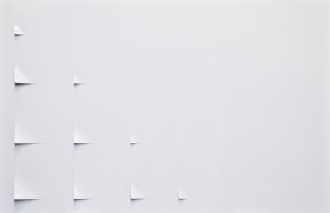 Abstract artwork featuring a series of intricately cut, overlapping white paper shapes arranged in a circular, spiral-like pattern. The layered elements create depth and shadow, adding dimension to the otherwise minimal composition on a white background. The piece invites viewers to explore subtle shifts in light and form, with a delicate interplay of curves and sharp angles.